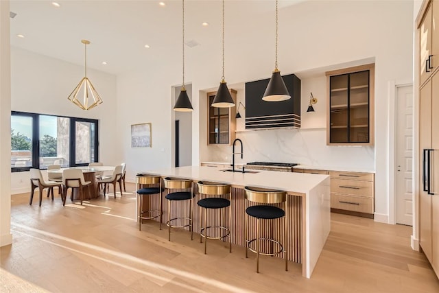 kitchen featuring custom exhaust hood, a sink, a towering ceiling, light countertops, and light wood-type flooring