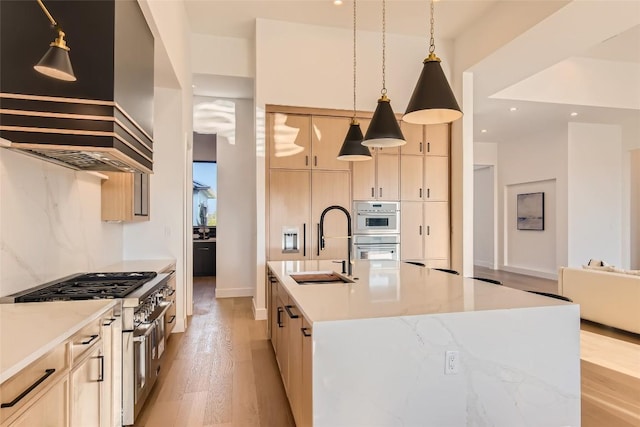 kitchen featuring stainless steel appliances, a sink, custom exhaust hood, light wood-type flooring, and hanging light fixtures