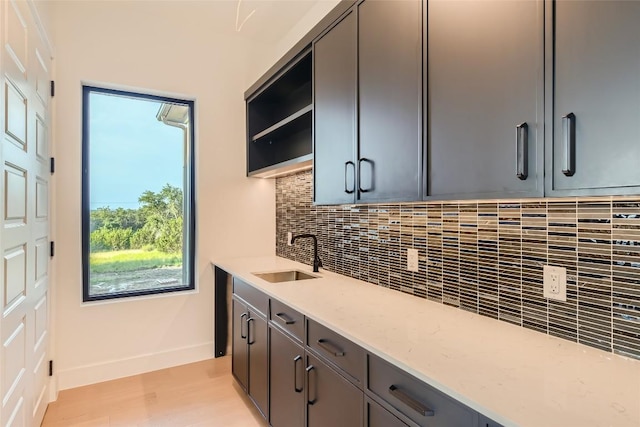 kitchen featuring a sink, tasteful backsplash, baseboards, light stone counters, and light wood-type flooring