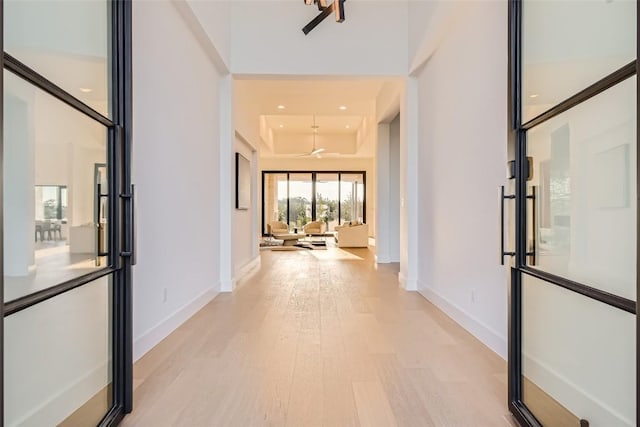 corridor with light wood finished floors, baseboards, a tray ceiling, and recessed lighting