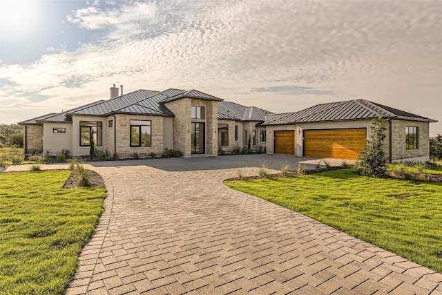 contemporary house with a standing seam roof, decorative driveway, metal roof, a chimney, and a front yard