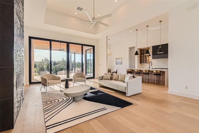 living area with light wood-style floors, ceiling fan, a fireplace, a towering ceiling, and recessed lighting