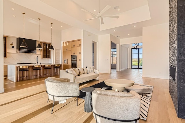 living area with light wood-style floors, ceiling fan, recessed lighting, a chandelier, and a towering ceiling