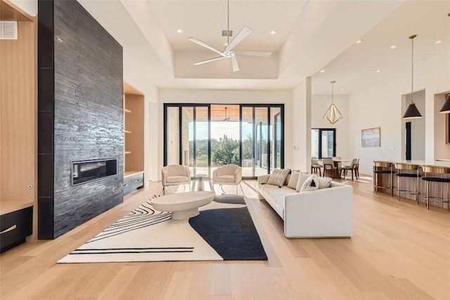 living room featuring a high ceiling, light wood-type flooring, a stone fireplace, recessed lighting, and a ceiling fan