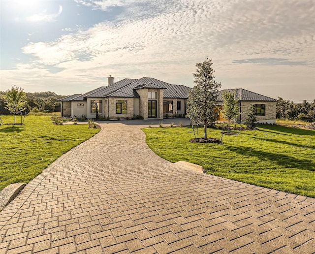 view of front of home with a chimney, a standing seam roof, stone siding, curved driveway, and a front lawn