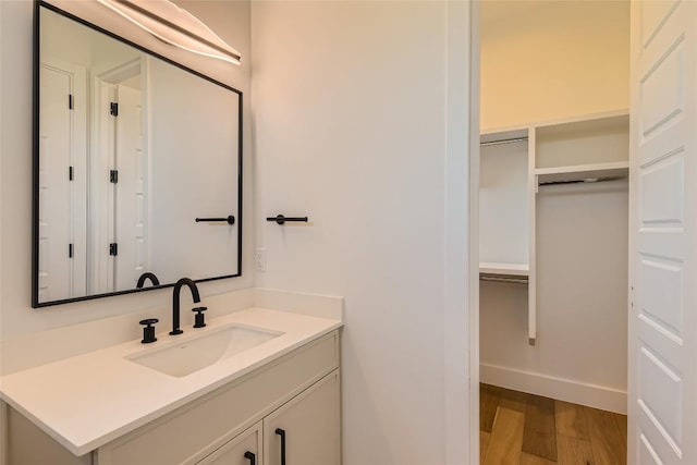bathroom featuring wood finished floors, vanity, baseboards, and a walk in closet