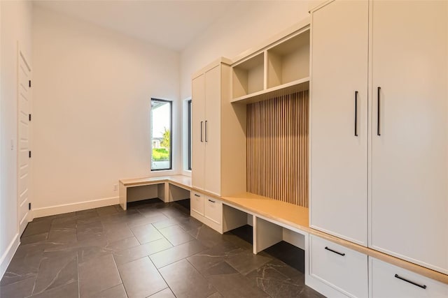 mudroom with built in study area, baseboards, and dark marble finish flooring