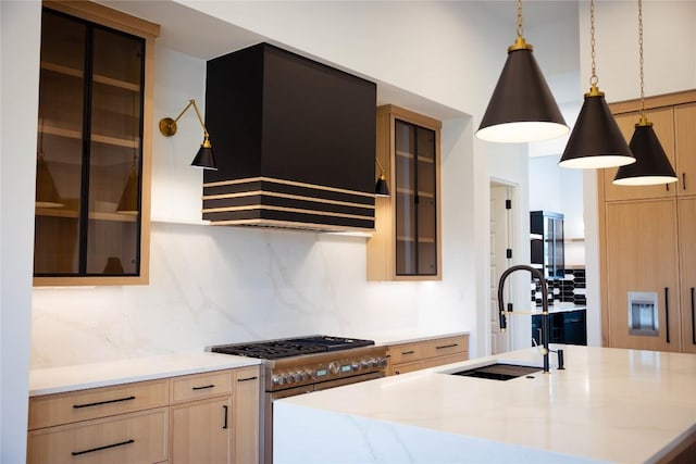 kitchen featuring stainless steel stove, premium range hood, a sink, tasteful backsplash, and light brown cabinetry