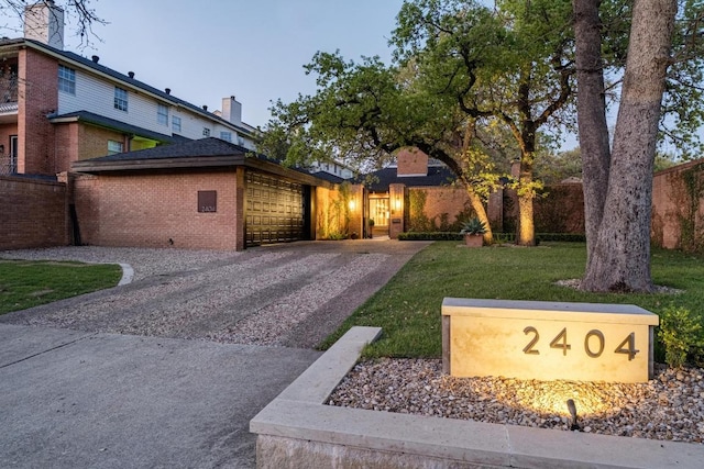 view of front of property featuring brick siding, an attached garage, gravel driveway, and a front lawn