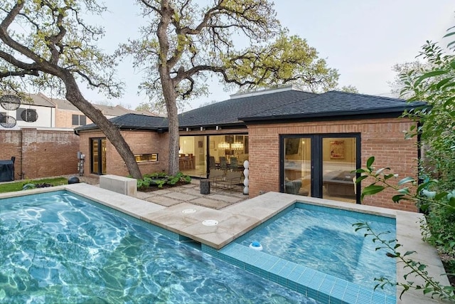 back of property featuring a shingled roof, brick siding, and a hot tub