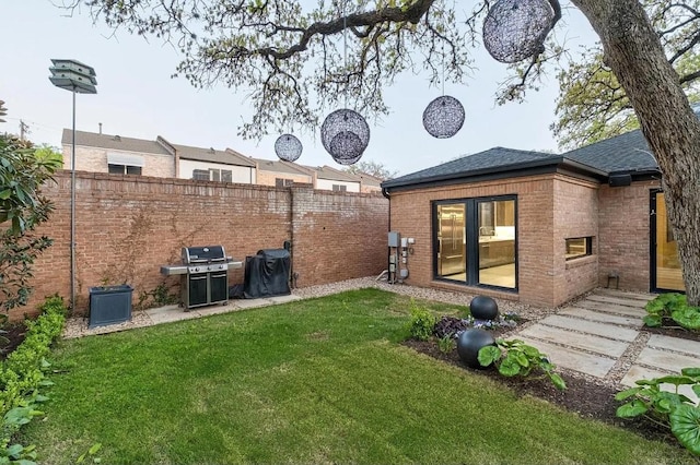 rear view of property with fence, roof with shingles, a yard, and brick siding