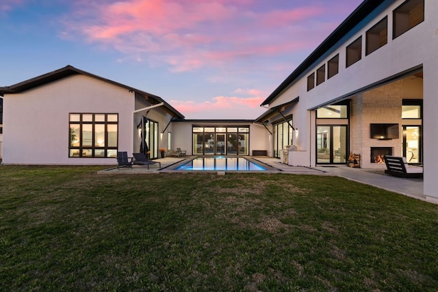 420 Waters Edge Cv, Dripping Springs, TX 78620 - back of property featuring a lawn, an outdoor pool, a patio area, stucco siding, and a lit fireplace