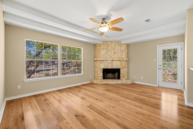 2300 Nevins Cv, Lago Vista, TX 78645 - unfurnished living room with light wood-type flooring, ceiling fan, a stone fireplace, and a raised ceiling