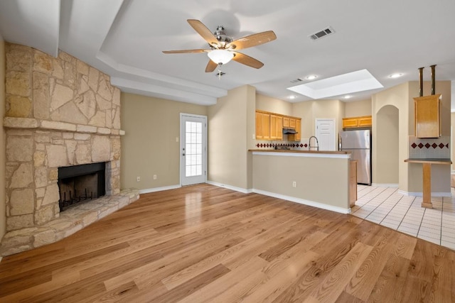 2300 Nevins Cv, Lago Vista, TX 78645 - unfurnished living room with a tray ceiling, a stone fireplace, ceiling fan, and light wood-style floors