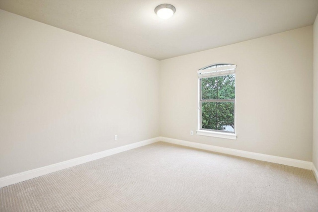 spare room featuring light carpet and baseboards