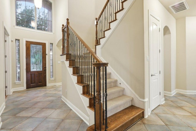 foyer entrance featuring light tile patterned floors, baseboards, visible vents, and stairway