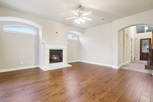 unfurnished living room featuring arched walkways, hardwood / wood-style floors, visible vents, and a wealth of natural light