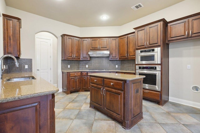 kitchen with arched walkways, a sink, tasteful backsplash, light stone countertops, and under cabinet range hood