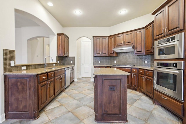kitchen featuring stainless steel appliances, arched walkways, a sink, tasteful backsplash, and under cabinet range hood