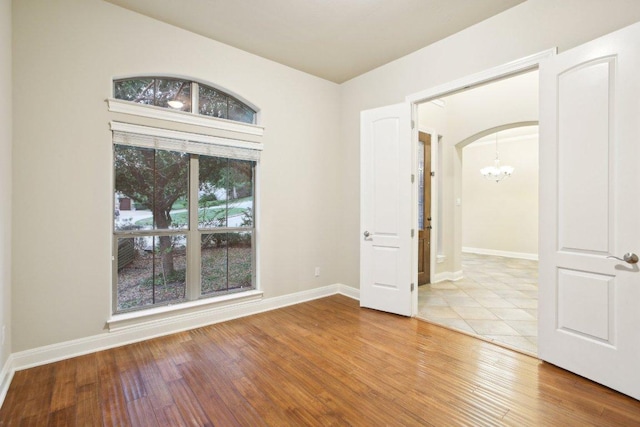 spare room with arched walkways, baseboards, a notable chandelier, and wood finished floors