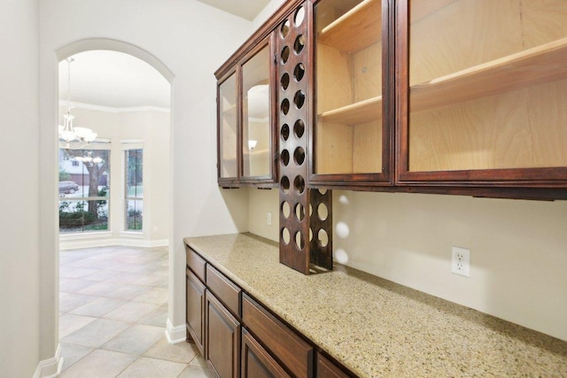 bar featuring crown molding, light tile patterned flooring, arched walkways, an inviting chandelier, and baseboards