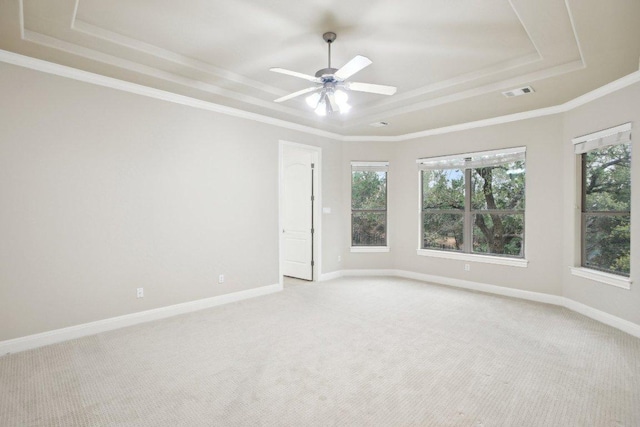 empty room with a raised ceiling, plenty of natural light, visible vents, and light carpet