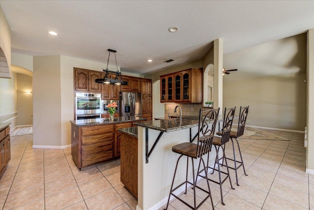 200 Matzig Cv, Buda, TX 78610 - kitchen with stainless steel appliances, brown cabinets, arched walkways, light tile patterned flooring, and dark stone countertops