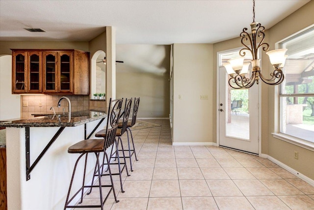 200 Matzig Cv, Buda, TX 78610 - kitchen with brown cabinetry, a kitchen breakfast bar, decorative backsplash, glass insert cabinets, and a chandelier