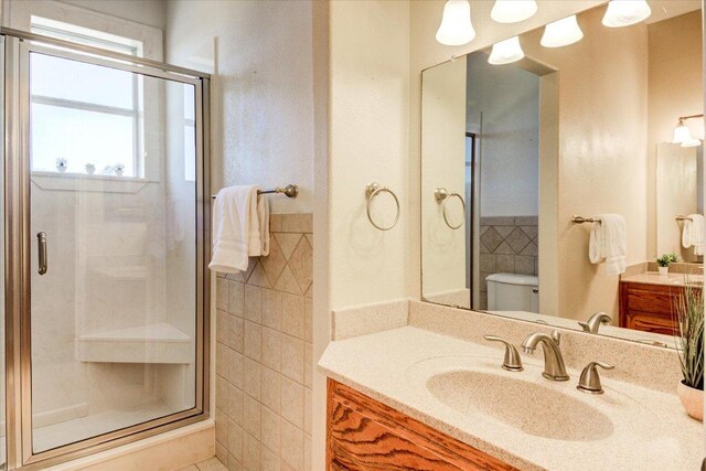 200 Matzig Cv, Buda, TX 78610 - bathroom with tile walls, a stall shower, toilet, vanity, and wainscoting