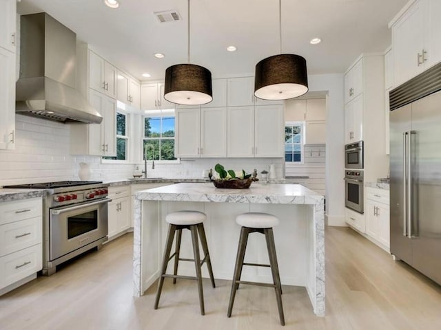 2000 Raleigh Ave, Austin, TX 78703 - kitchen featuring high quality appliances, wall chimney exhaust hood, decorative backsplash, white cabinetry, and a kitchen island