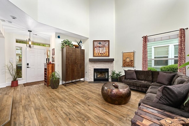 living room featuring a high ceiling, hardwood / wood-style flooring, a stone fireplace, and baseboards