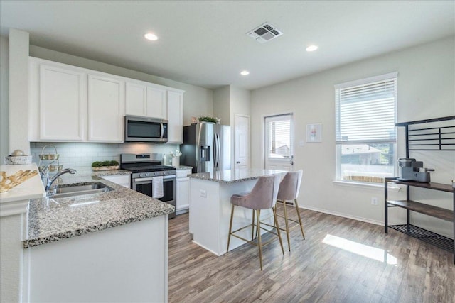 kitchen featuring appliances with stainless steel finishes, a sink, light wood finished floors, a kitchen island, and white cabinetry