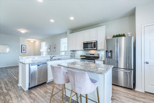 kitchen with appliances with stainless steel finishes, a sink, a peninsula, light wood finished floors, and recessed lighting