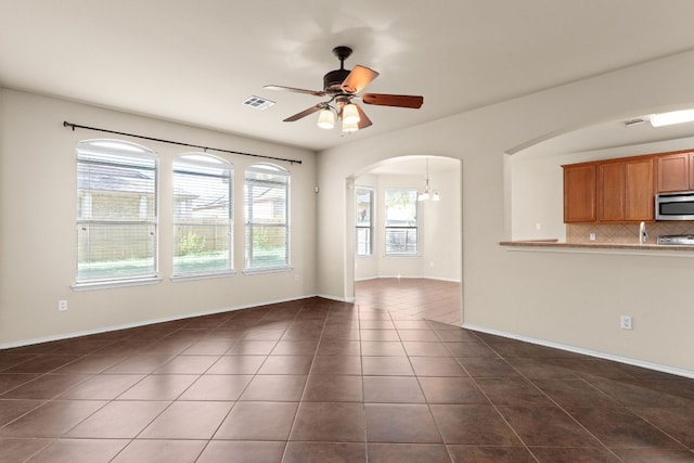 5405 English Oak Dr, Killeen, TX 76542 - unfurnished living room with dark tile patterned floors, baseboards, visible vents, arched walkways, and ceiling fan with notable chandelier