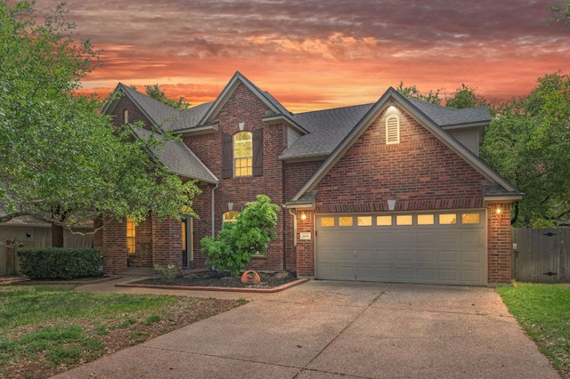 traditional home featuring driveway, brick siding, fence, a garage, and roof with shingles
