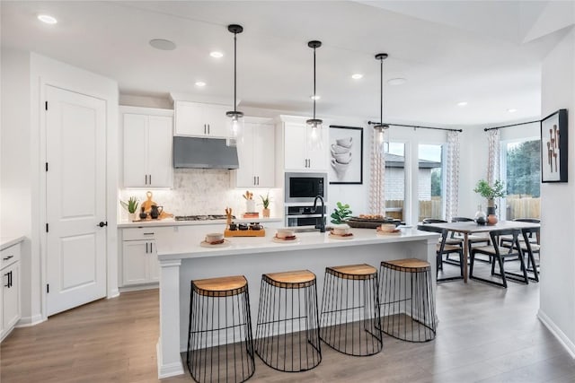 120 Amber Oak Ln, Georgetown, TX 78628 - kitchen featuring under cabinet range hood, appliances with stainless steel finishes, light wood finished floors, backsplash, and light countertops