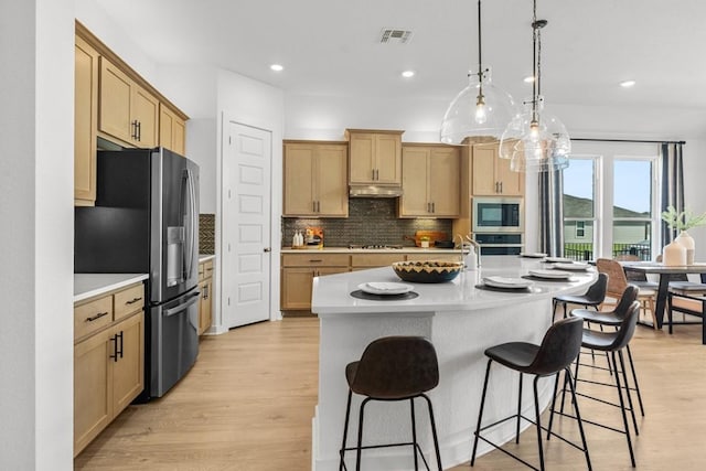 13615 Thomas Wheeler Way, Manor, TX 78653 - kitchen featuring appliances with stainless steel finishes, under cabinet range hood, a kitchen breakfast bar, light countertops, and decorative backsplash
