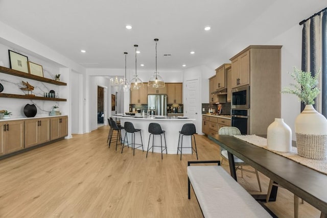 13615 Thomas Wheeler Way, Manor, TX 78653 - kitchen with stainless steel appliances, a breakfast bar, decorative backsplash, light countertops, and light wood-style flooring