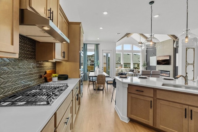 13615 Thomas Wheeler Way, Manor, TX 78653 - kitchen featuring stainless steel gas stovetop, under cabinet range hood, open floor plan, a sink, and backsplash