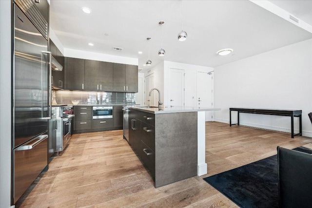 222 W Ave Unit 1213, Austin, TX 78701 - kitchen featuring high end appliances, light wood finished floors, pendant lighting, tasteful backsplash, and an island with sink