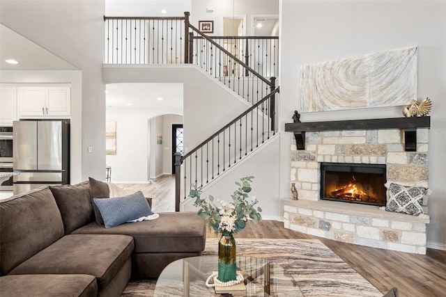 5621 Cypress Ranch Blvd, Spicewood, TX 78669 - living room with arched walkways, wood finished floors, a towering ceiling, stairway, and a stone fireplace