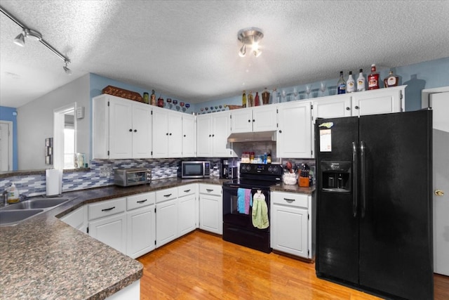 kitchen with under cabinet range hood, light wood finished floors, dark countertops, and black appliances