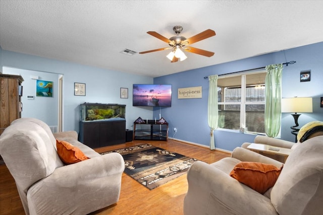 living room featuring a textured ceiling, a ceiling fan, visible vents, wood finished floors, and baseboards