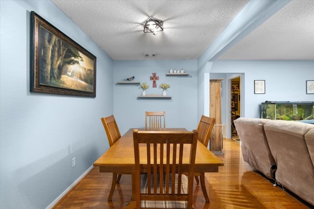 dining area featuring a textured ceiling, wood finished floors, baseboards, and visible vents