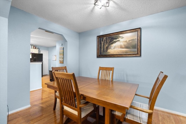 dining room with light wood-style floors, baseboards, a textured ceiling, and arched walkways
