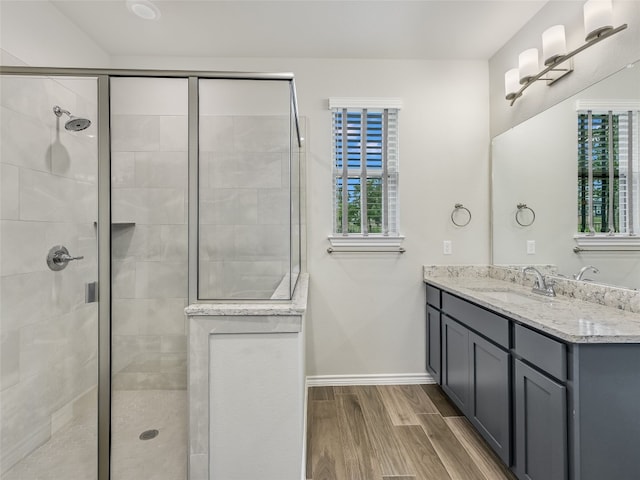 bathroom with baseboards, wood finished floors, vanity, and a tile shower