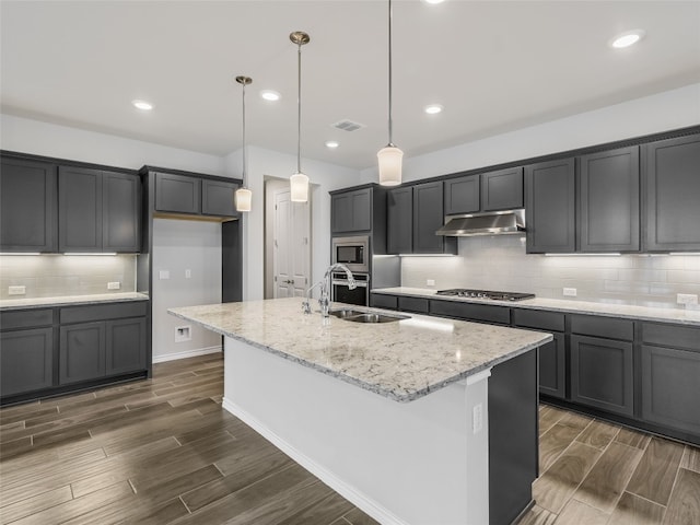 kitchen with dark wood finished floors, an island with sink, under cabinet range hood, and a sink