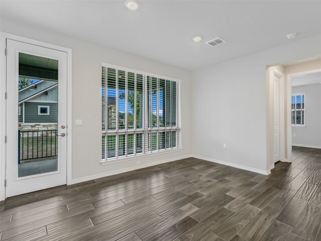 empty room with visible vents, baseboards, dark wood-style flooring, and a healthy amount of sunlight