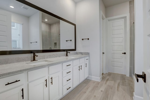 full bathroom with double vanity, wood finished floors, a stall shower, a sink, and baseboards