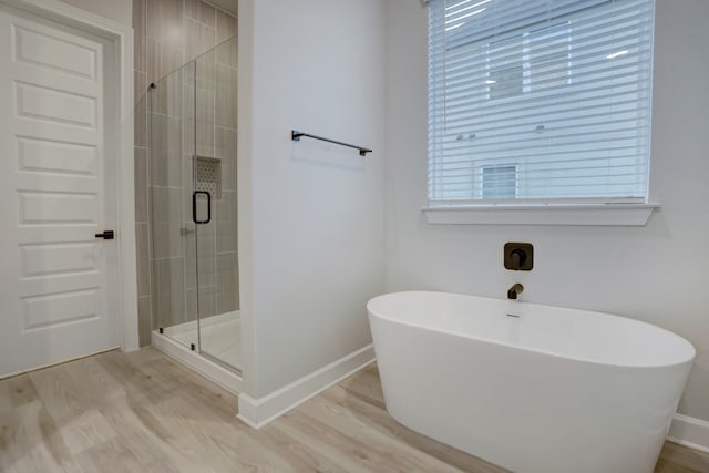 bathroom with wood finished floors, a wealth of natural light, a shower stall, a soaking tub, and baseboards